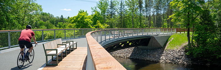 Cycliste traversant la passerelle surplombant la rivière au parc Chauveau par une journée estivale ensoleillée